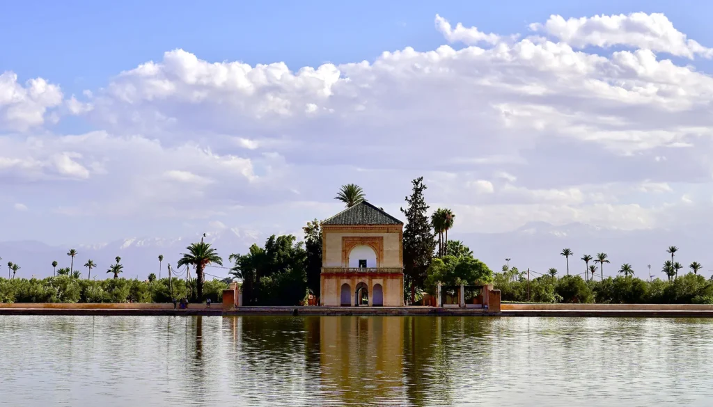 A serene image of the Menara Gardens pavilion in Marrakech, with its reflection in the water and the High Atlas Mountains in the background.