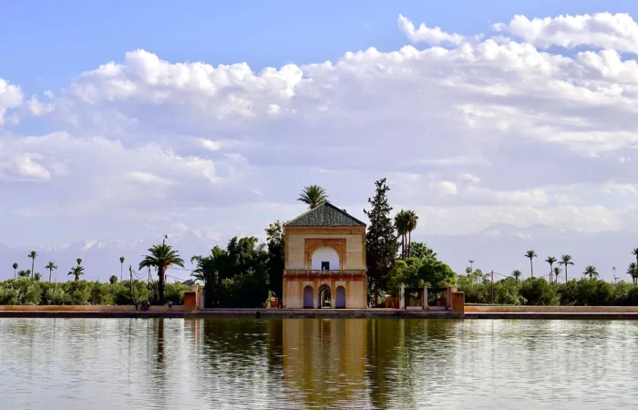 A serene image of the Menara Gardens pavilion in Marrakech, with its reflection in the water and the High Atlas Mountains in the background.