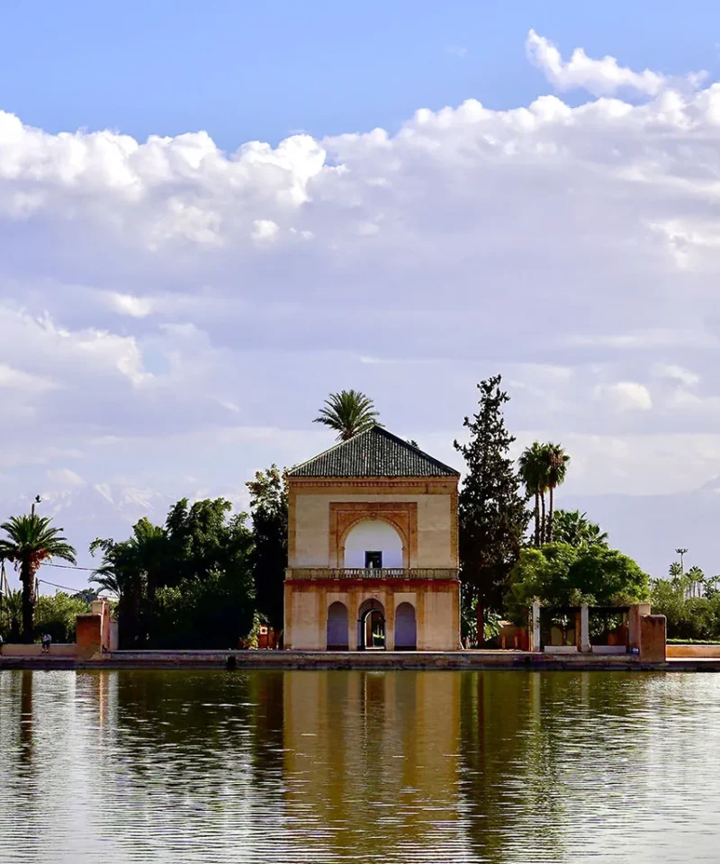 A serene image of the Menara Gardens pavilion in Marrakech, with its reflection in the water and the High Atlas Mountains in the background.