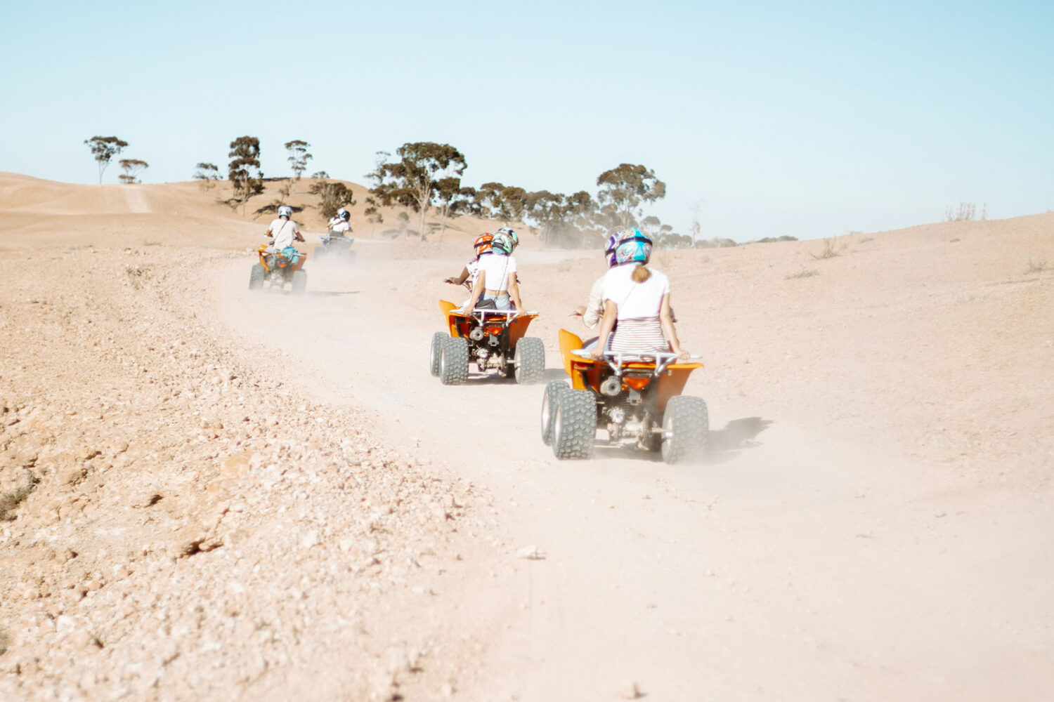 Group of travelers riding quad bikes on a desert trail with clear skies in the background.