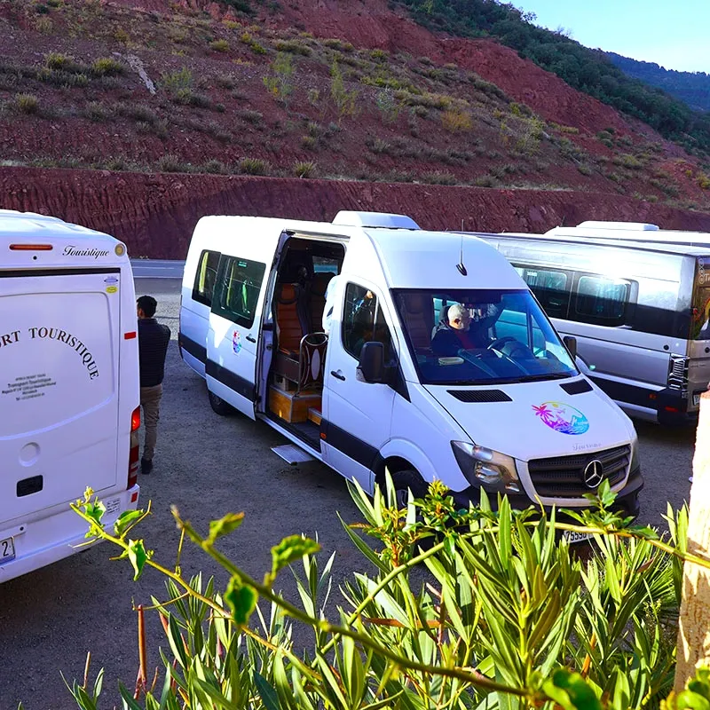 Modern tourist transport vans parked near a scenic hillside, used for Morocco Tours & Transfers to provide comfortable and safe travel experiences.