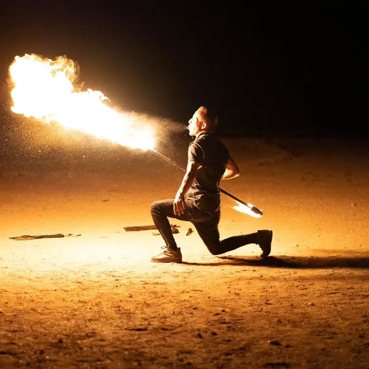 A fire performer breathes a burst of flames during a captivating dinner spectacle in the Agafay Desert at night