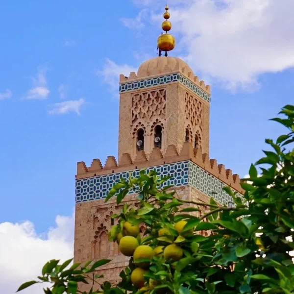 The Koutoubia Mosque in Marrakech with intricate tile details and greenery in the foreground under a bright blue sky.