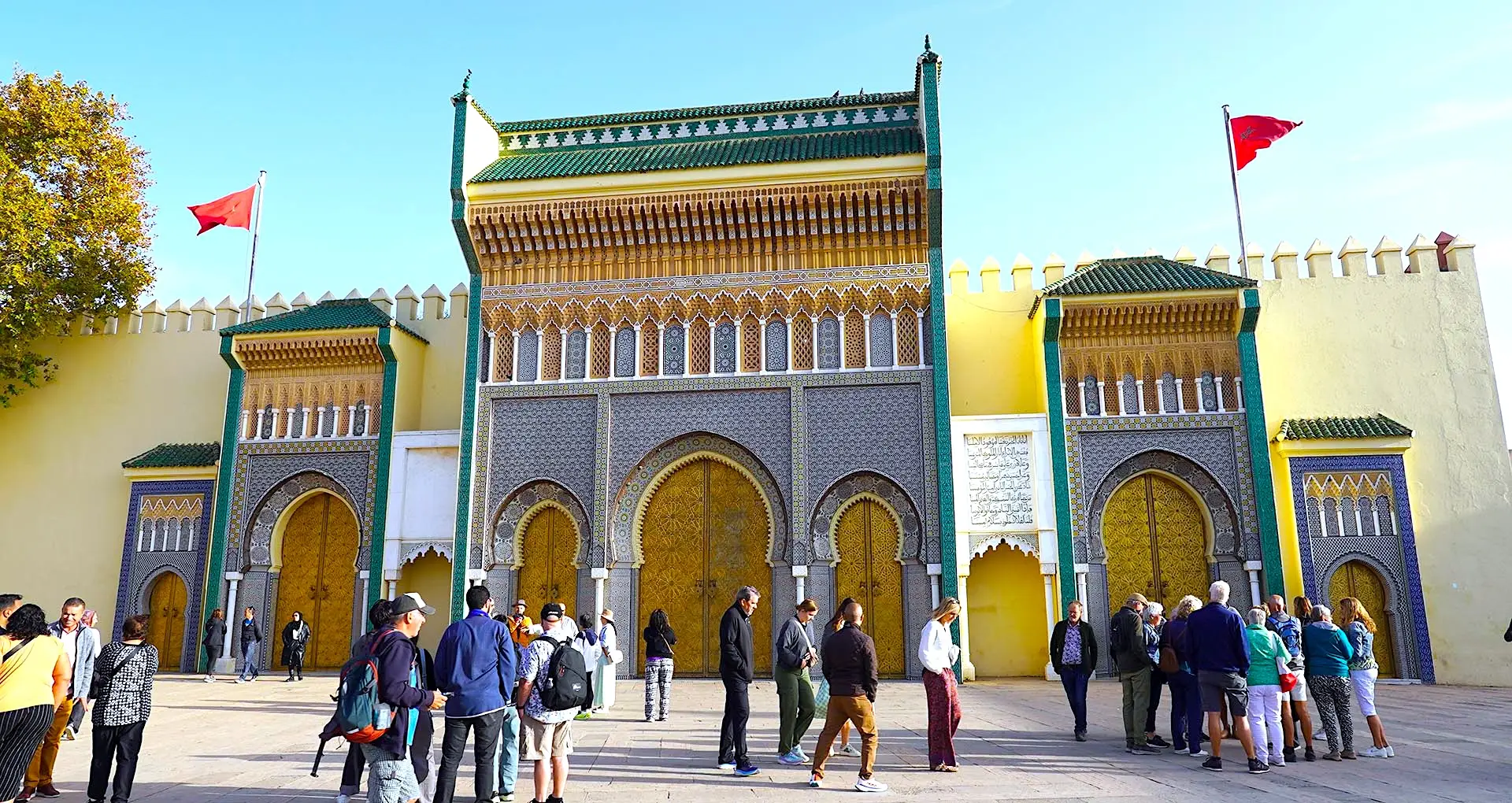 Golden gates of the Royal Palace in Fes, Morocco, with tourists walking nearby on a Morocco Tours & Transfers excursion